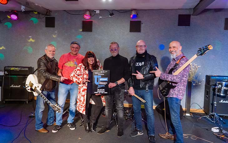 6 people from a rock banding standing and pointing to the UPRAWR charity concert poster.